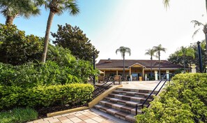 A hotel with a staircase leading to the entrance, surrounded by lush greenery and palm trees.