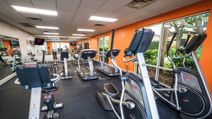 A gym with various cardio equipment, including treadmills and elliptical machines, and a large window providing a view of the outdoors. - Townhome Jacuzzi Grill 10 min Disney (Kissimmee)