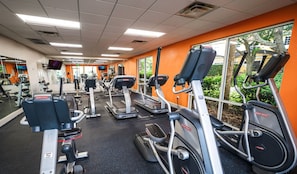 A gym with various cardio equipment, including treadmills and elliptical machines, and a large window providing a view of the outdoors. - Townhome Jacuzzi Grill 10 min Disney (Kissimmee)