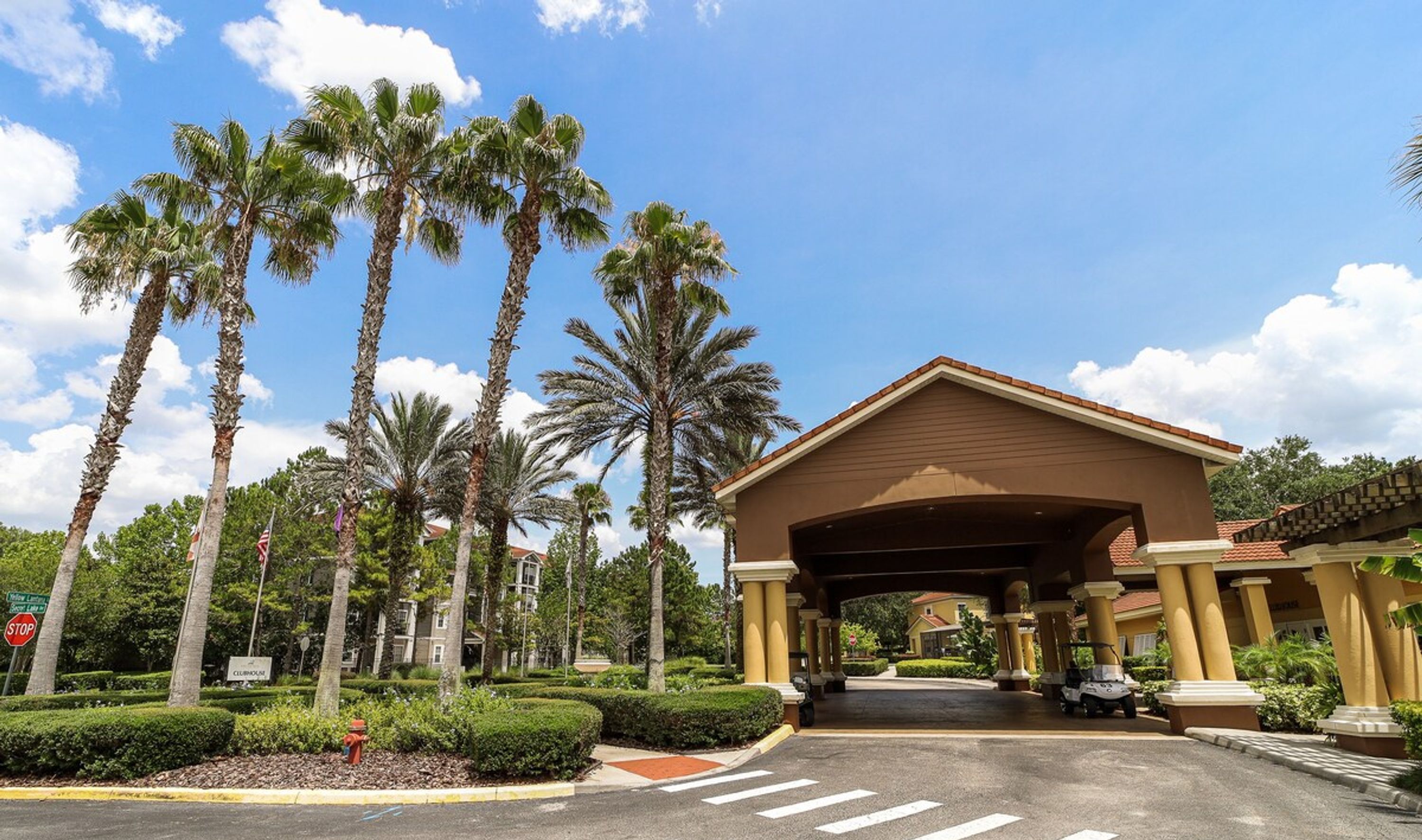A hotel entrance with a covered walkway, palm trees, and a stop sign.