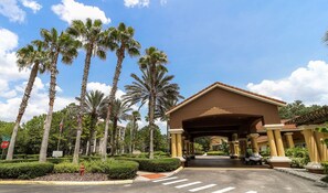 A hotel entrance with a covered walkway, palm trees, and a stop sign.