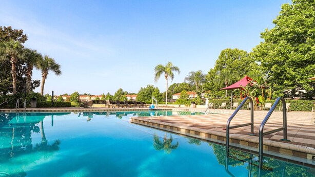A clear swimming pool with lounge chairs and umbrellas, surrounded by palm trees and a clear sky. - Townhome Jacuzzi Grill 10 min Disney (Kissimmee)