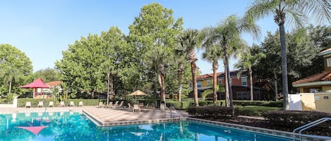 A swimming pool surrounded by palm trees and lounge chairs, with a clear blue sky above.