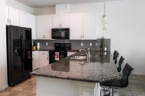 A modern kitchen with white cabinets, a black refrigerator, a microwave, and a granite countertop.