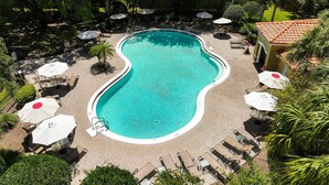 Vista aérea de una piscina rodeada de sillas de descanso y sombrillas, con un patio empedrado y vegetación al fondo.