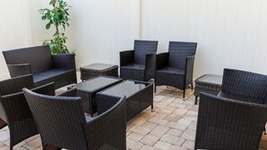 Un patio con mobiliario de mimbre, incluyendo sillas y mesas, y una planta en maceta.