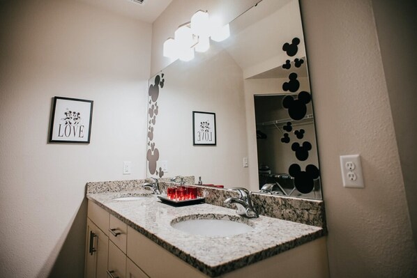 A bathroom with a granite countertop, two sinks, a mirror with Mickey Mouse cutouts, and two framed signs that say "LOVE".