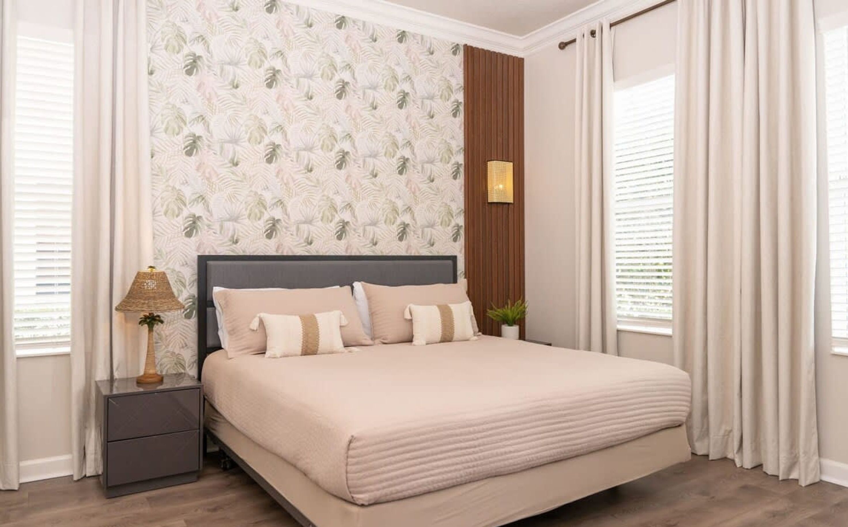 Quarto com cama, mesa de cabeceira, abajur e um vaso com planta.