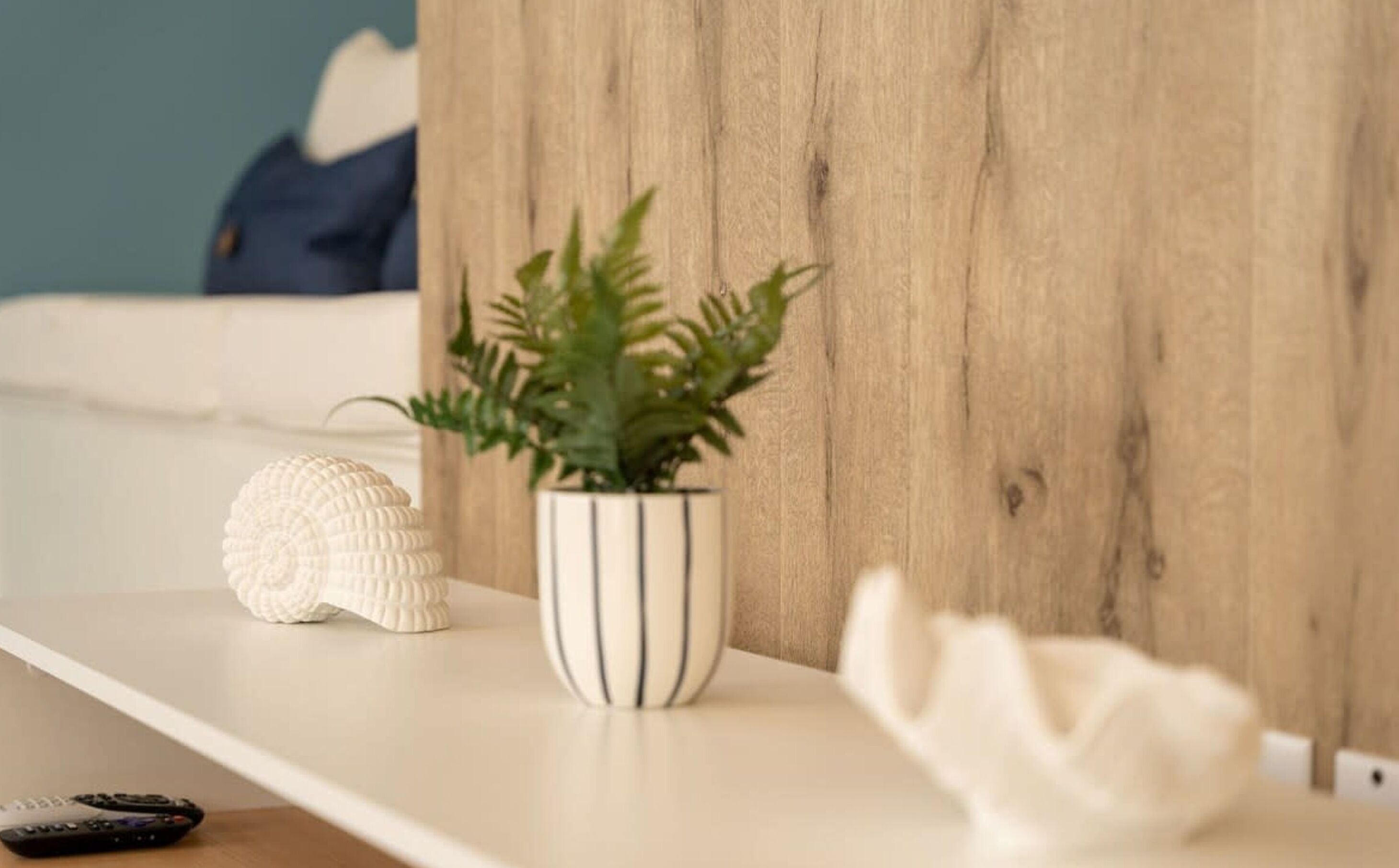 A white shelf with a potted plant, a white decorative object, and a remote control.
