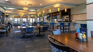 Un restaurante amplio con varias mesas y sillas, una zona de bar y una cocina visible al fondo.