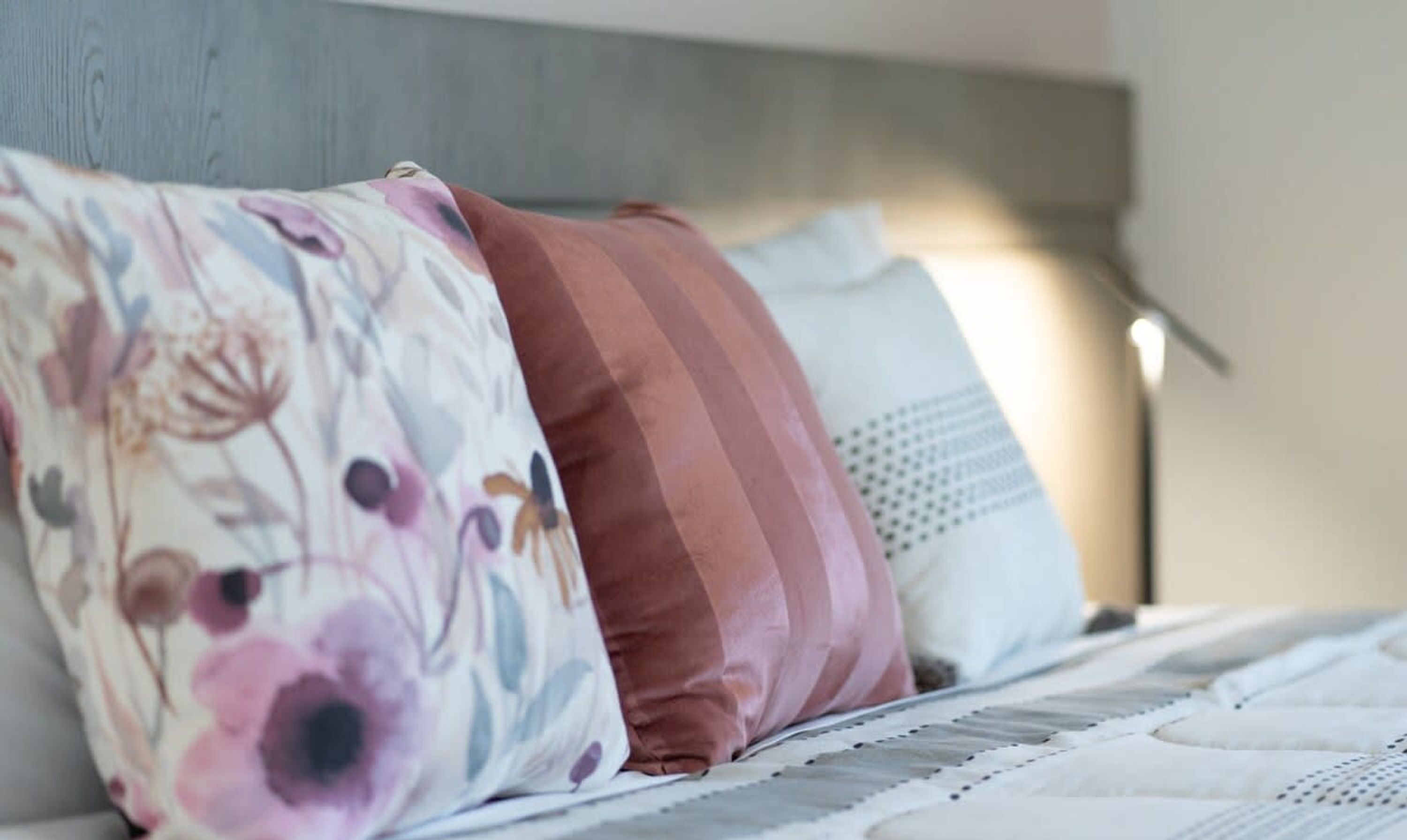 Una cama con un almohadón estampado, un almohadón de color uniforme y un almohadón blanco con diseño de lunares.