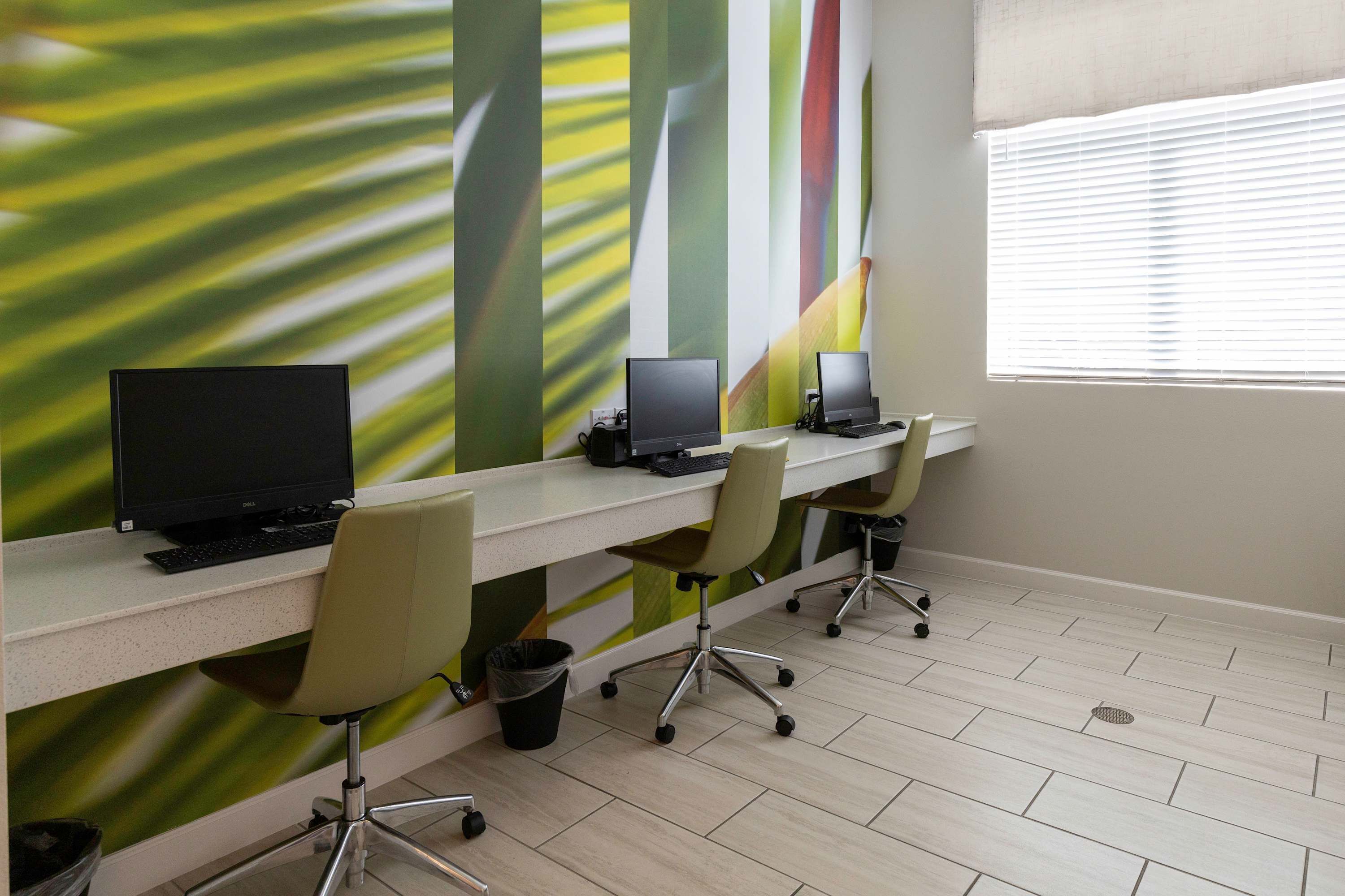 Un espacio de oficina moderno con tres escritorios, cada uno con una computadora y una silla. La habitación tiene un piso de baldosas limpias y un ventanal con persianas.