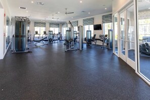 A gym with various exercise machines, large windows, and a ceiling fan. - Amazing House Near the Parks (Kissimmee)