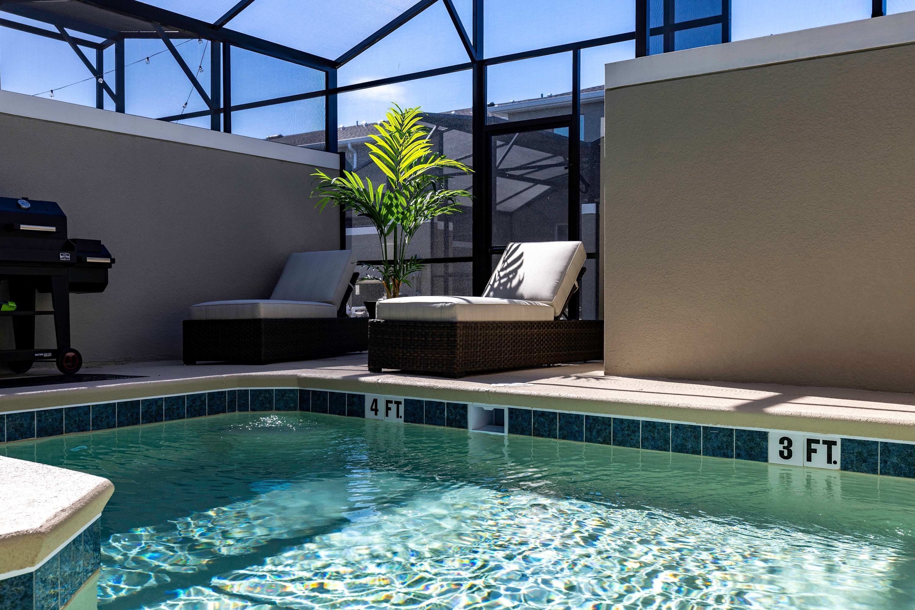 Una piscina con superficie d'acqua limpida, una sedia a sdraio, un barbecue e una pianta in vaso.