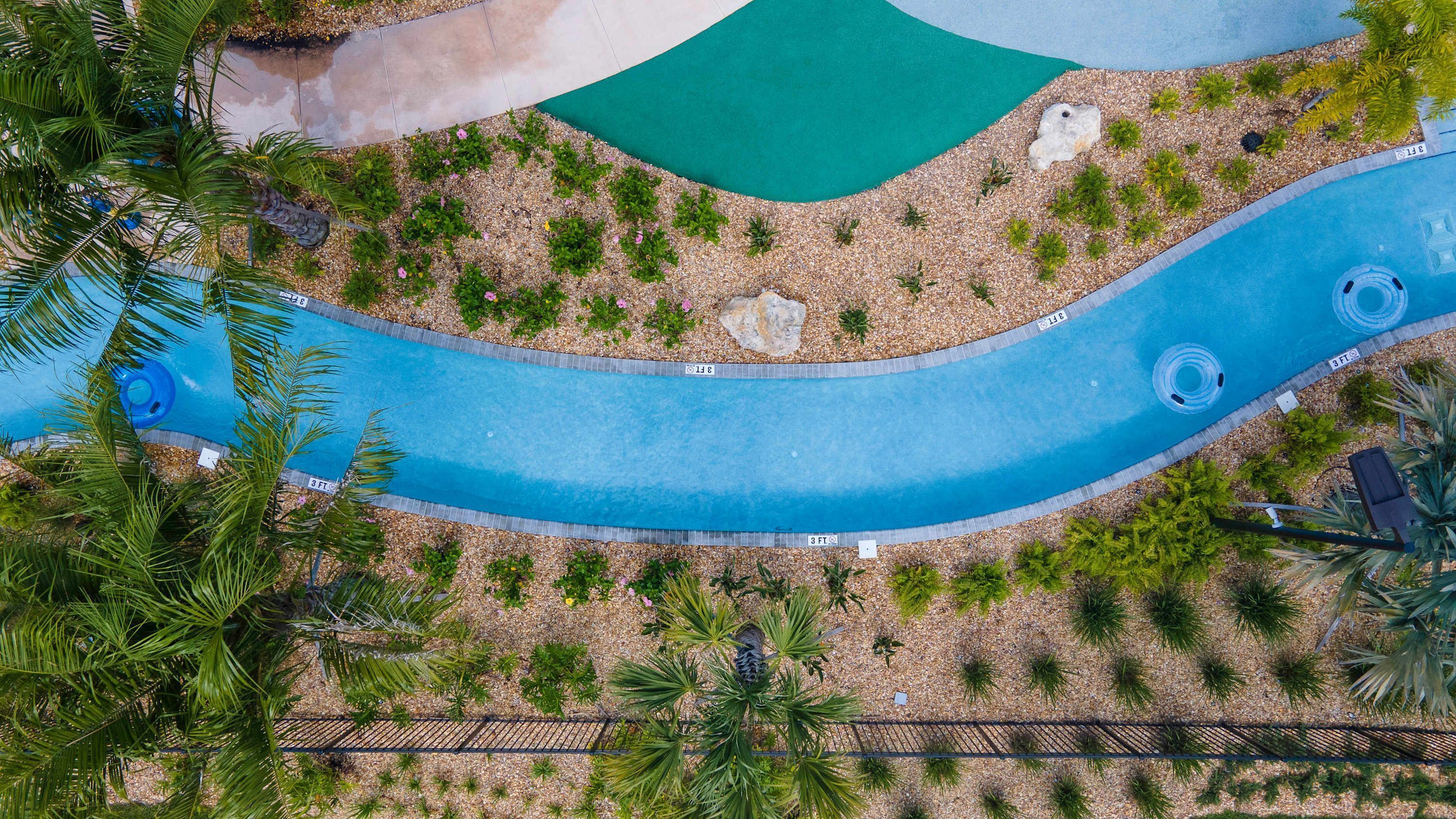 An aerial view of a swimming pool area with a winding water feature, surrounded by pebbles and greenery.