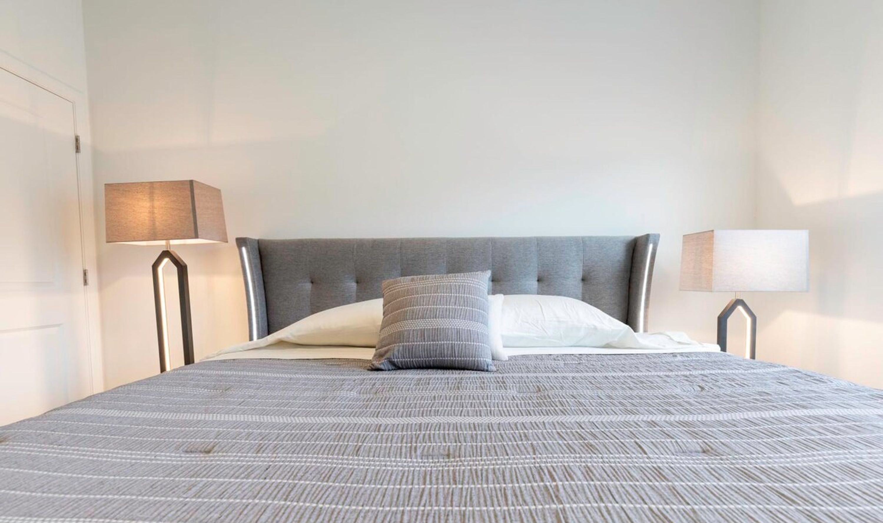 A neatly made bed with a grey headboard and two bedside lamps.