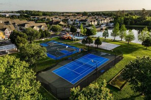 An aerial view of a residential area with a tennis court, a playground, and a body of water.