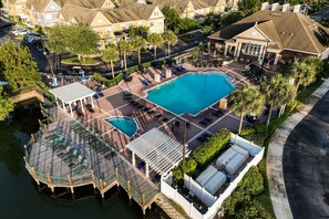 An aerial view of a hotel with a large central pool, a smaller pool, and a deck area with lounge chairs and umbrellas.
