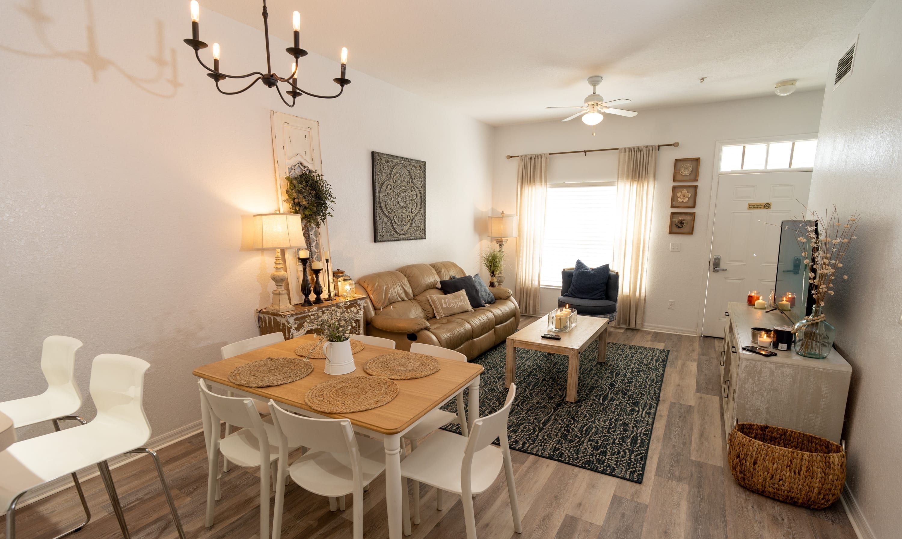 A cozy living room with a brown leather sofa, white chairs, a wooden dining table, and a ceiling fan.