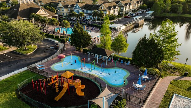 A playground with slides and climbing structures, a covered seating area, and a lake view. - Apartment Minutes From Disney (Kissimmee)