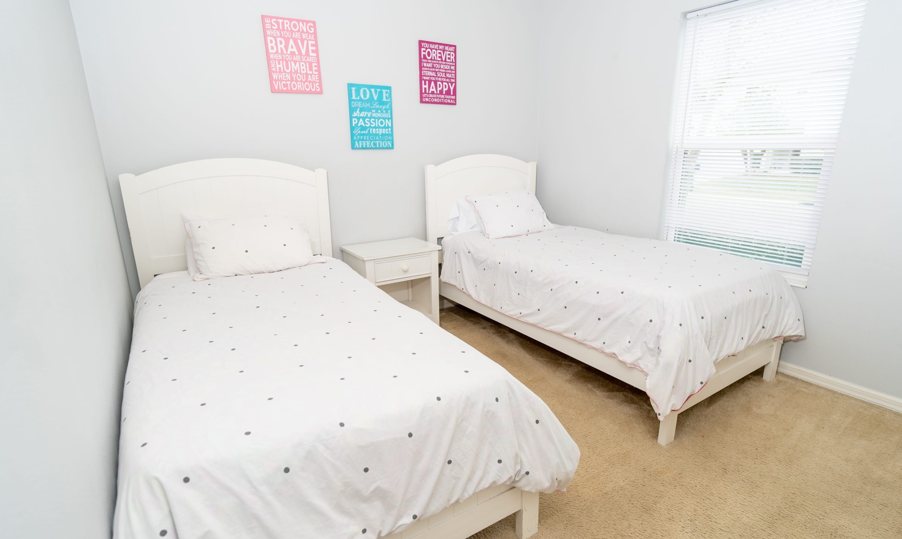 Een slaapkamer met twee eenpersoonsbedden, wit beddengoed, een nachtkastje en motiverende posters aan de muur.