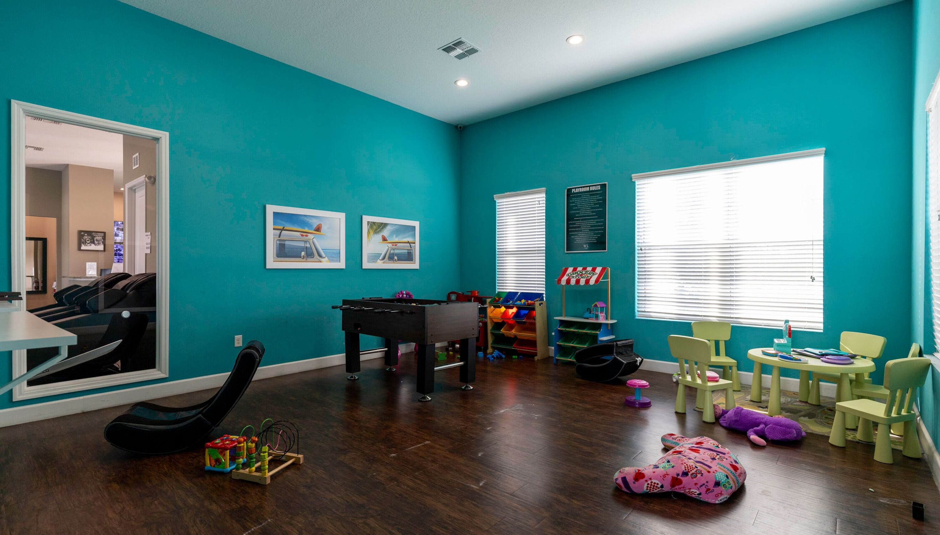 A teal-colored room with a foosball table, playroom signs, and children's toys.