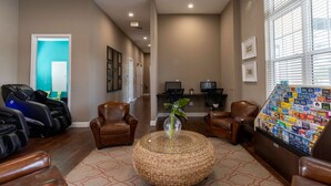 A lobby with leather chairs, a massage chair, a woven ottoman, a reception desk, and a wall with various magazines.
