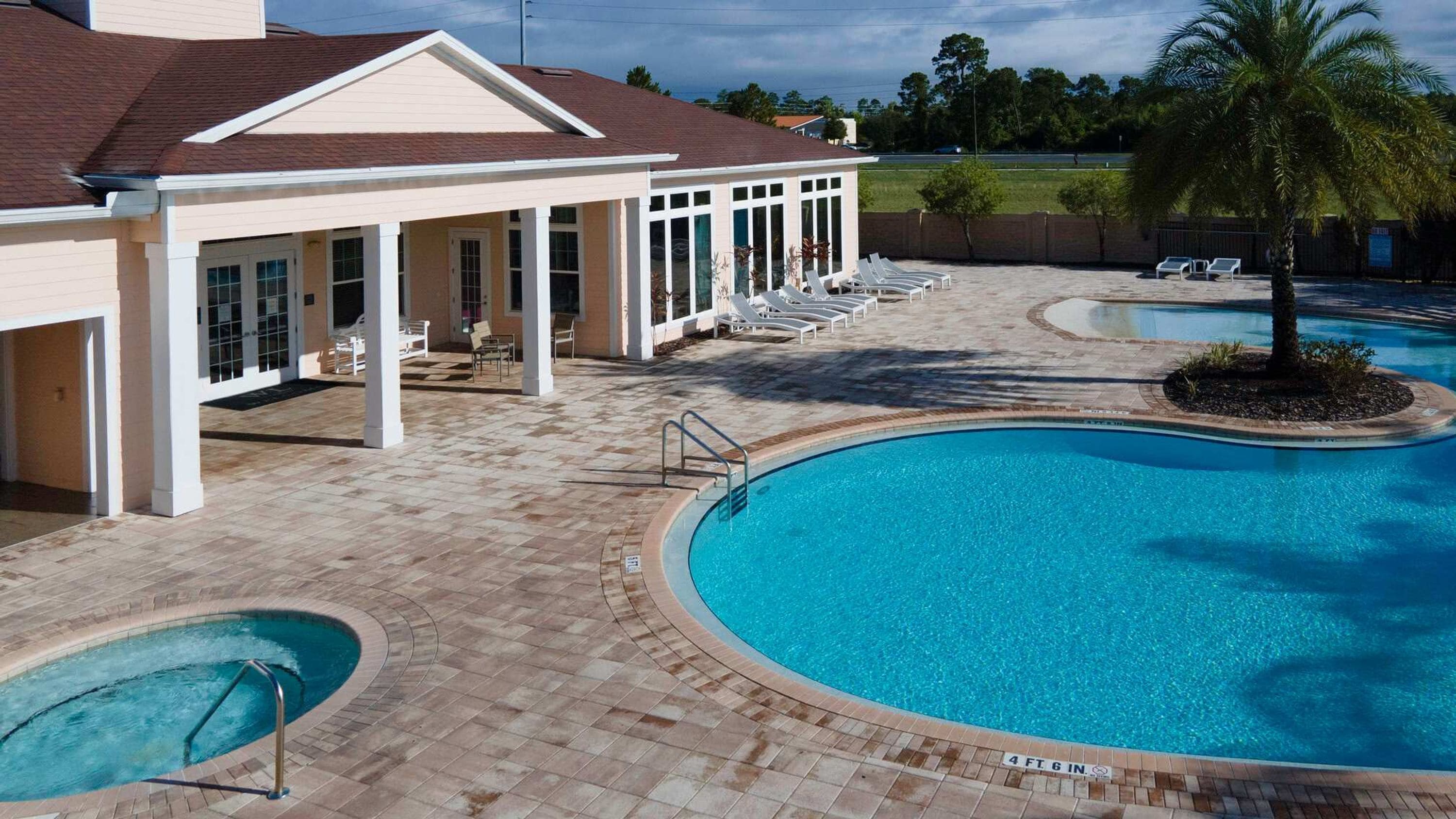 Ein Schwimmbecken mit Sonnenterrasse, Liegestühlen und einem überdachten Patio-Bereich.