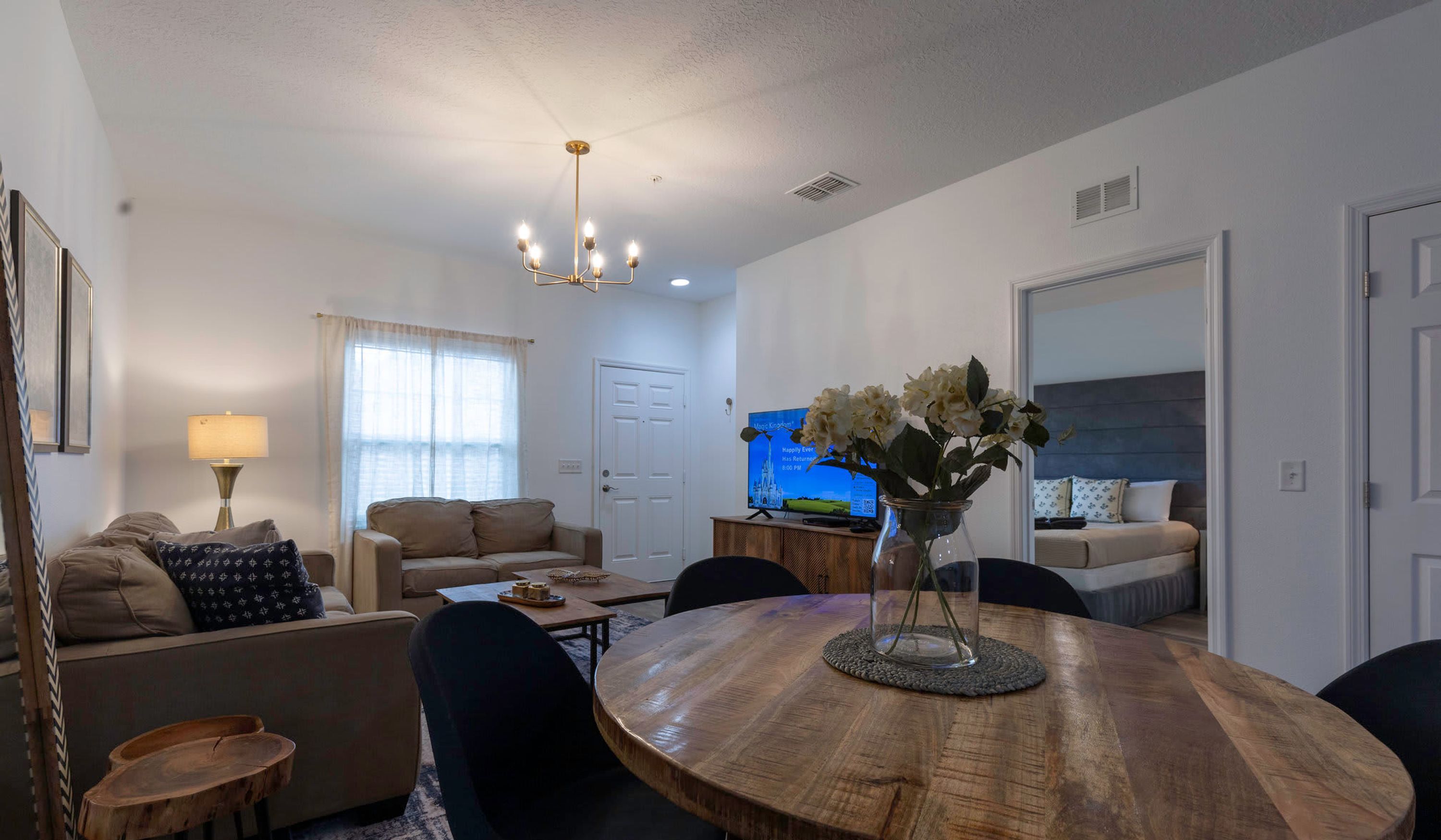 A living room with a wooden dining table, beige sofas, and a chandelier.