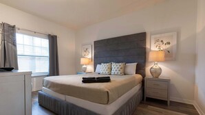 A bedroom with a large bed, two bedside tables, a window with curtains, and a wall-mounted lamp. - Fabulous Townhome Near the Parks (Kissimmee)