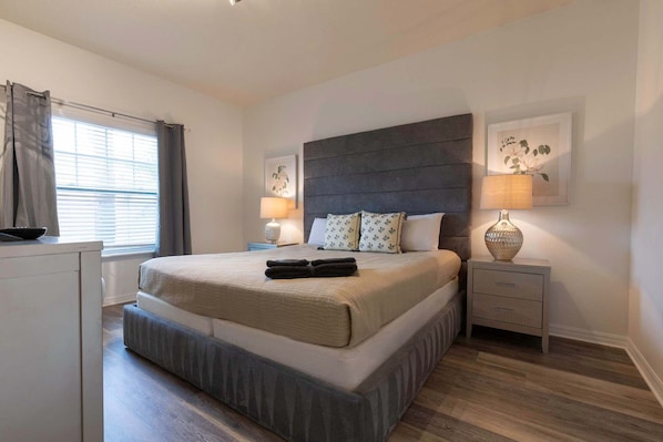 A bedroom with a large bed, two bedside tables, a window with curtains, and a wall-mounted lamp. - Fabulous Townhome Near the Parks (Kissimmee)