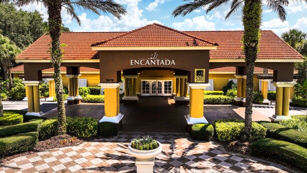 Entrada de hotel con pavimento a cuadros, palmeras y un letrero que dice 'ENCANTADA'.