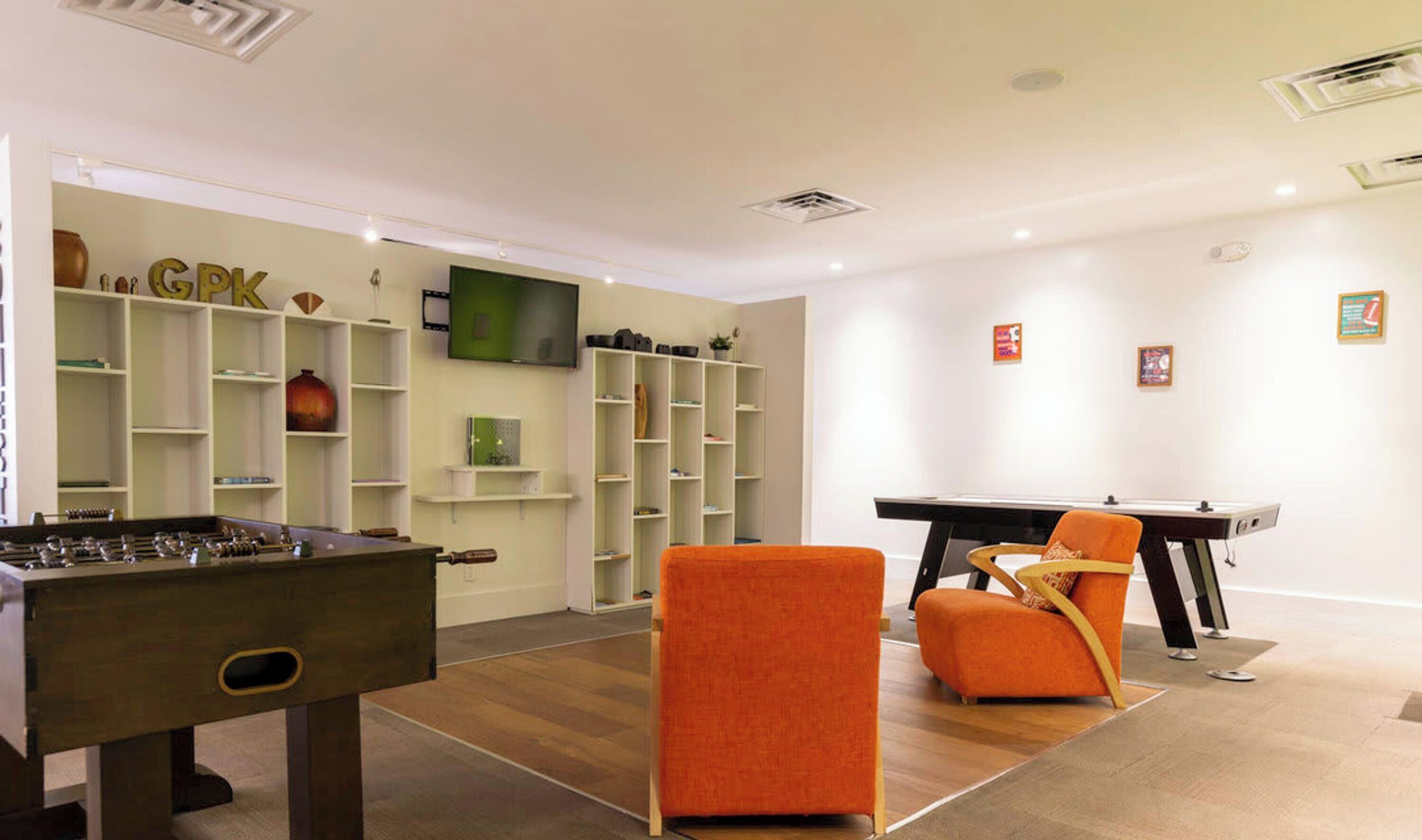 A room with a foosball table, a pool table, and a comfortable orange chair.