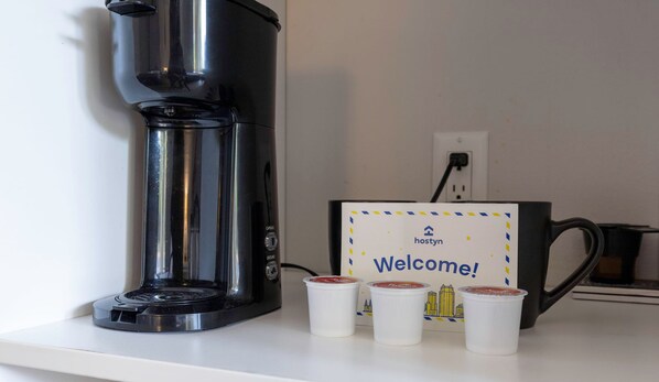Una cafetera, un letrero de bienvenida y tres vasos desechables sobre una encimera.
