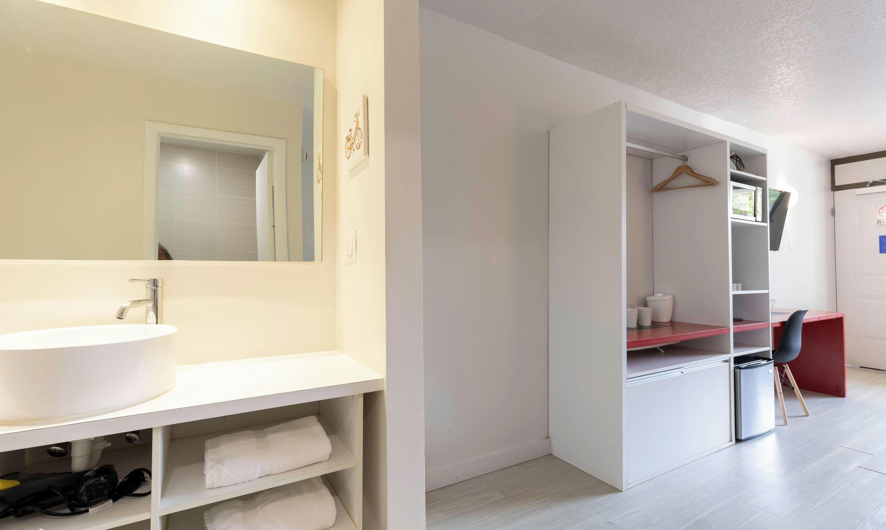 Un baño moderno con un lavabo grande, espejo y un vestidor con estantes y una silla.