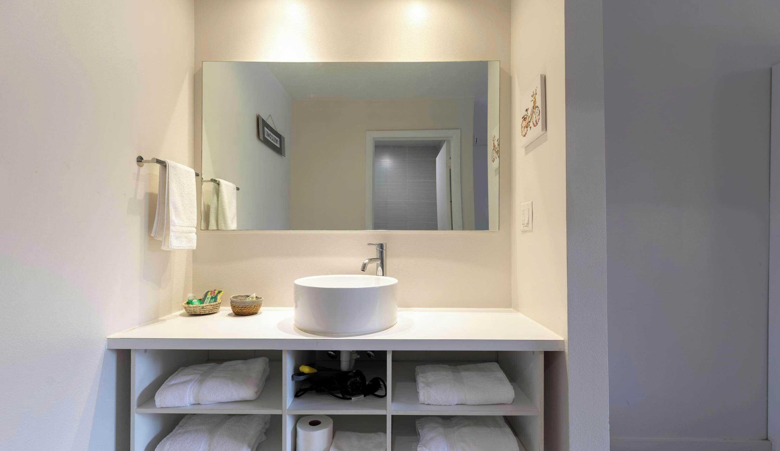 A bathroom with a white sink, mirror, and shelves with towels.