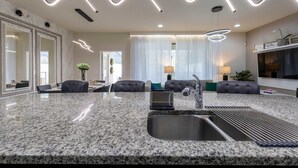 A modern kitchen with granite countertops, a built-in sink, and contemporary lighting fixtures. - Fabulous Townhouse Near to Disney (Kissimmee)