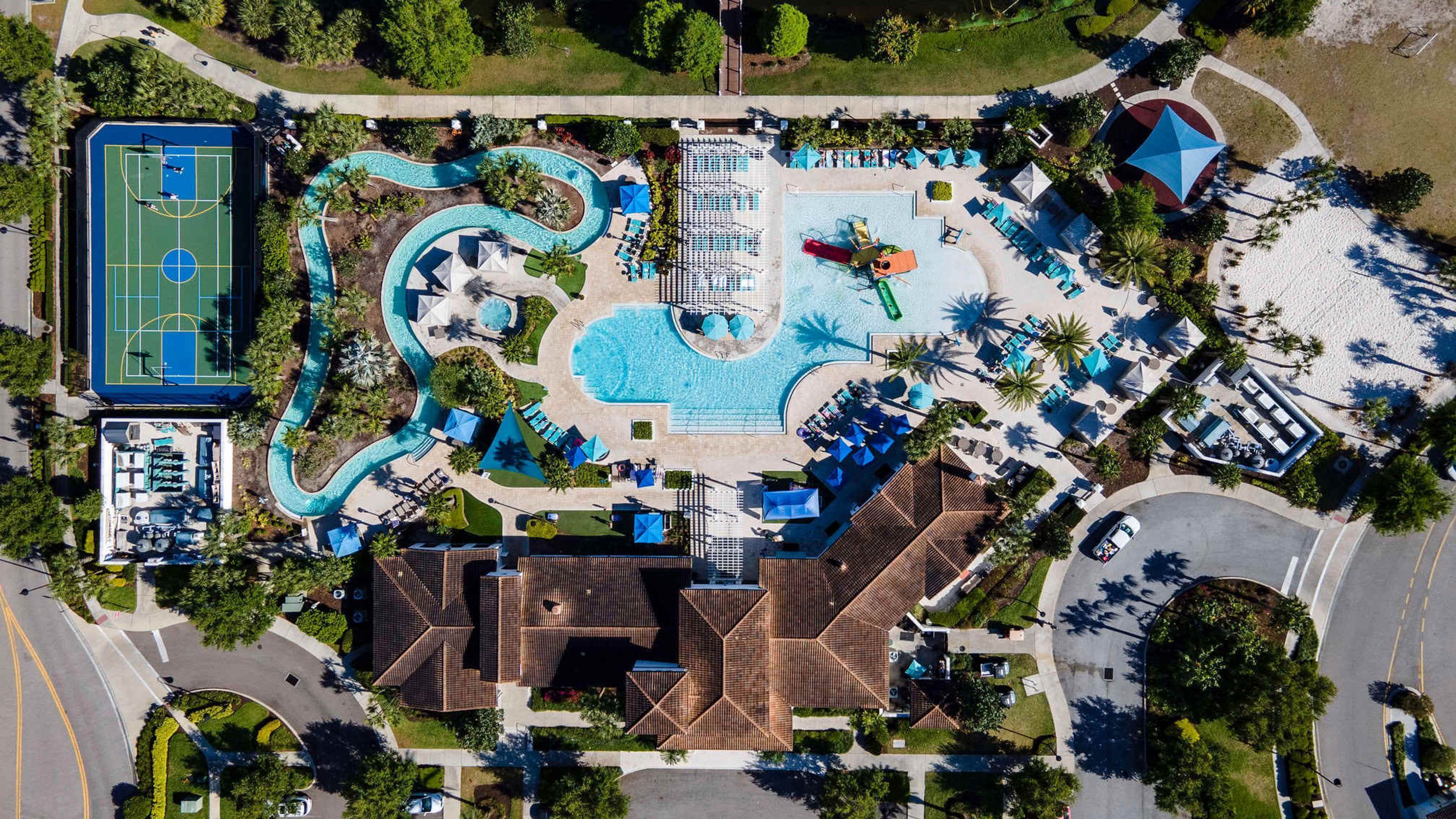 An aerial view of a resort with a swimming pool, a tennis court, and a beach area.