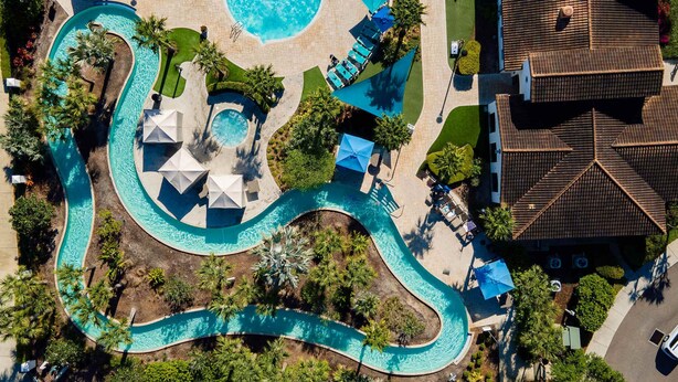 An aerial view of a resort with a winding pool, lounge chairs, and palm trees. - Fabulous Townhouse Near to Disney (Kissimmee)