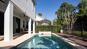 Une piscine avec une terrasse, un espace couvert et une maison dotée d’un porche grillagé.