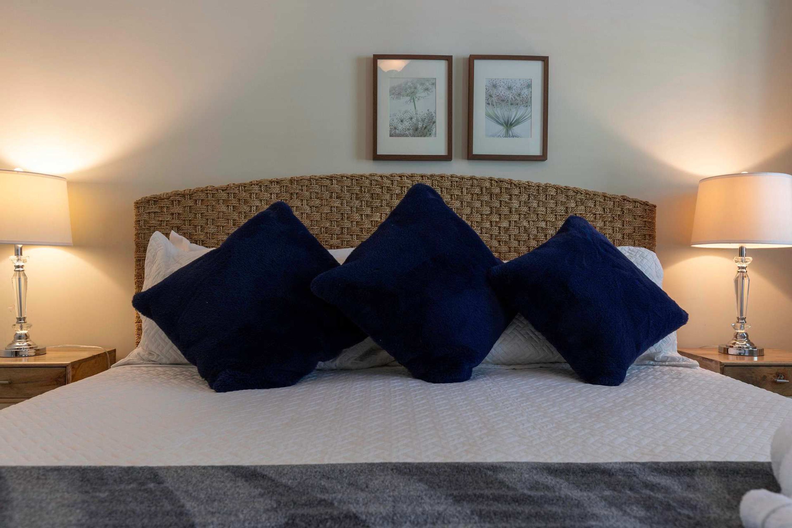 A bed with a woven headboard, two framed pictures on the wall, and two bedside lamps.