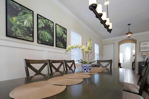 Une salle à manger avec une longue table, des chaises, une plante en pot et des tableaux encadrés accrochés au mur.