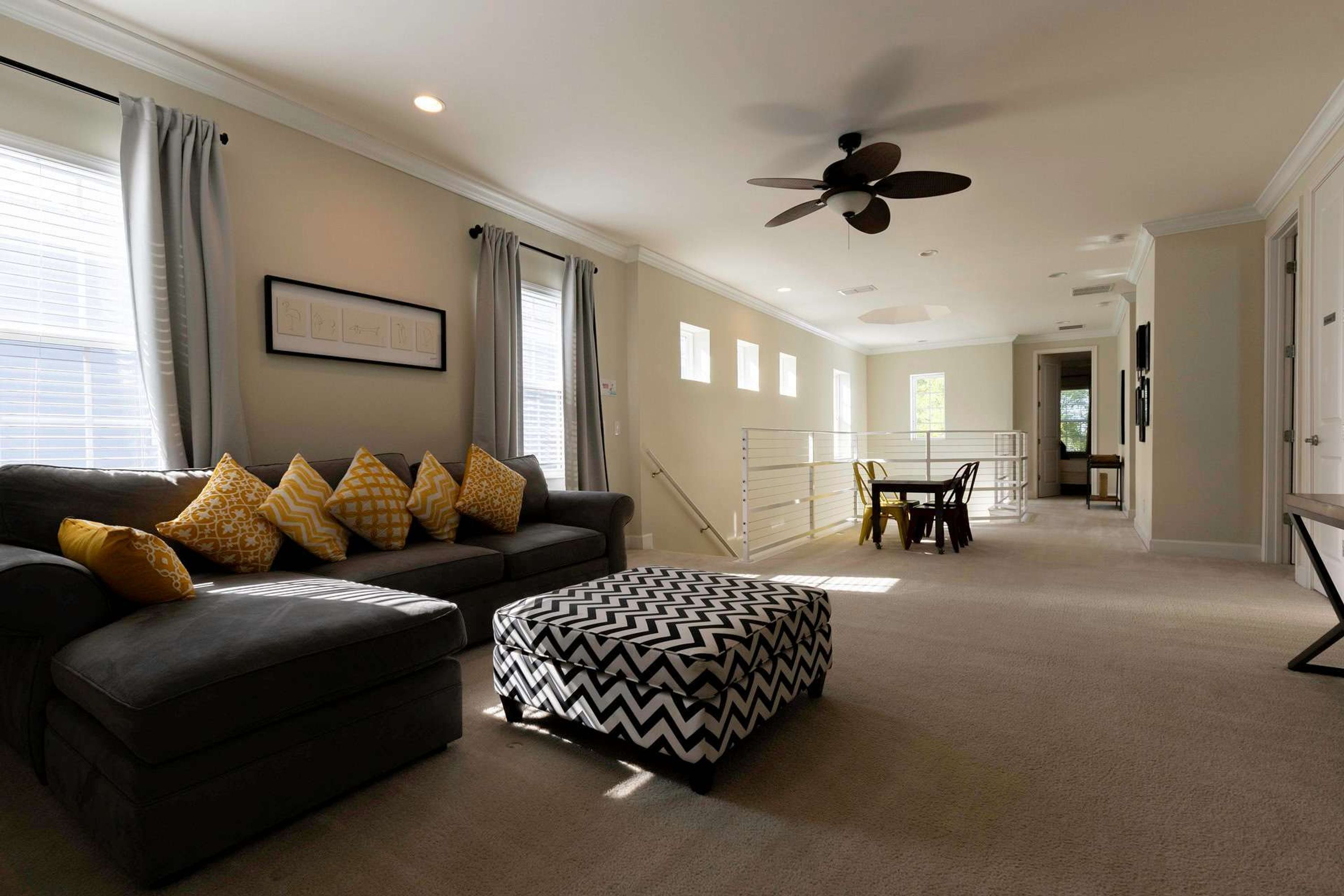 A spacious living room with a dark sofa, ottoman, and a ceiling fan.
