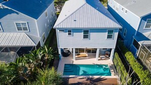 Une maison à deux étages avec un jardin devant, une piscine et un patio couvert.
