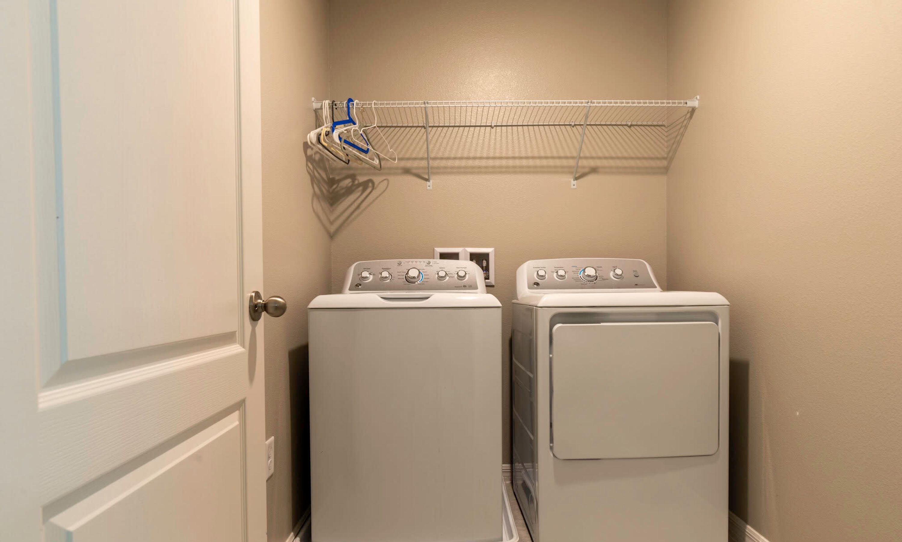 A laundry room with two front-loading washers and a metal drying rack above them.