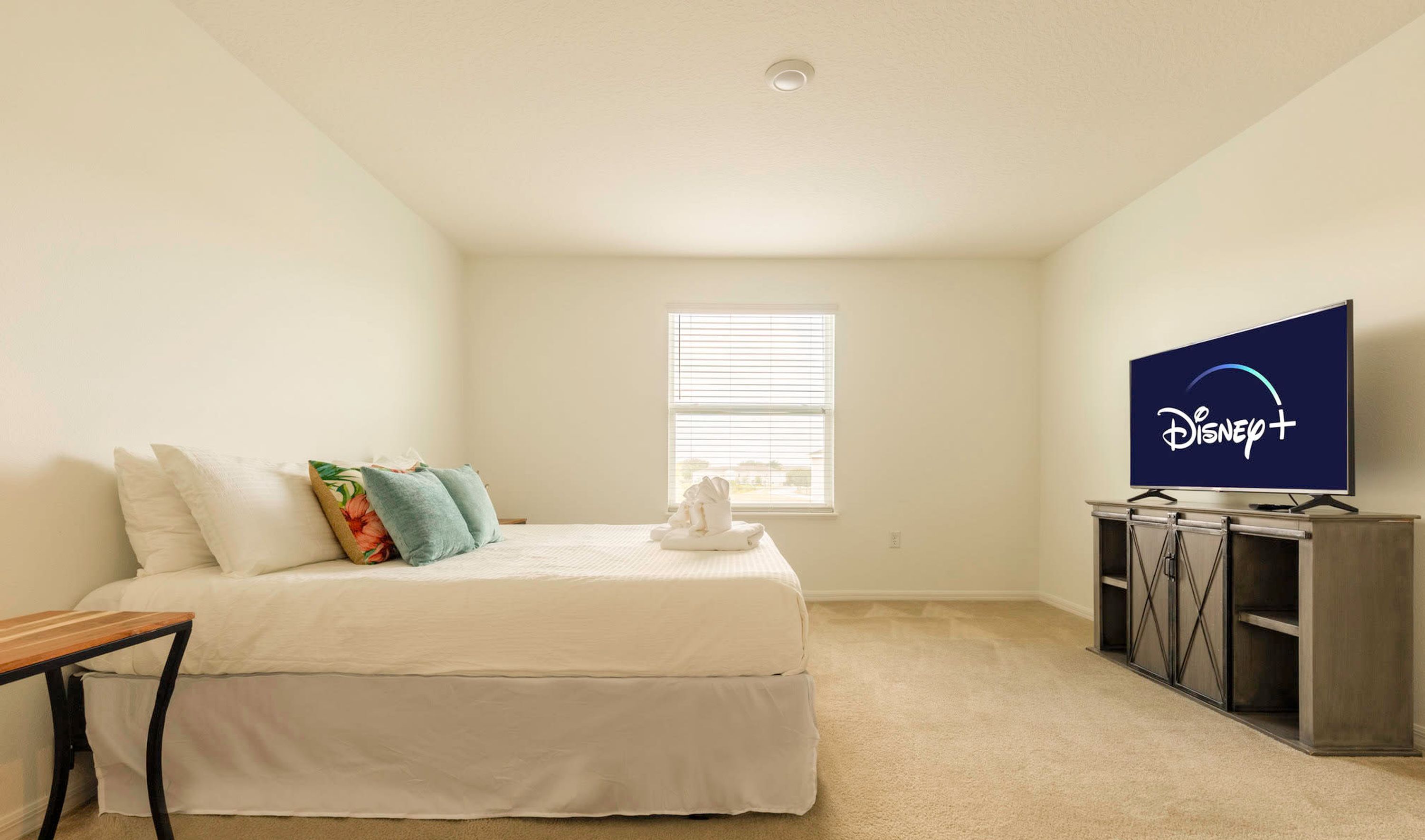 A bedroom with a bed, pillows, a TV, and a window.