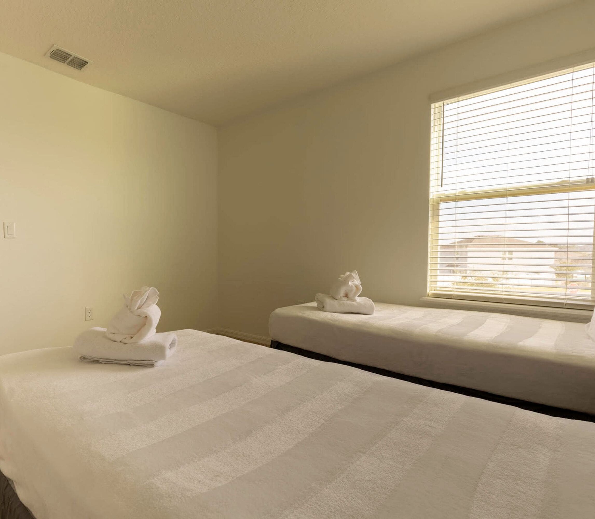 A hotel room with two beds, each with a neatly folded towel.