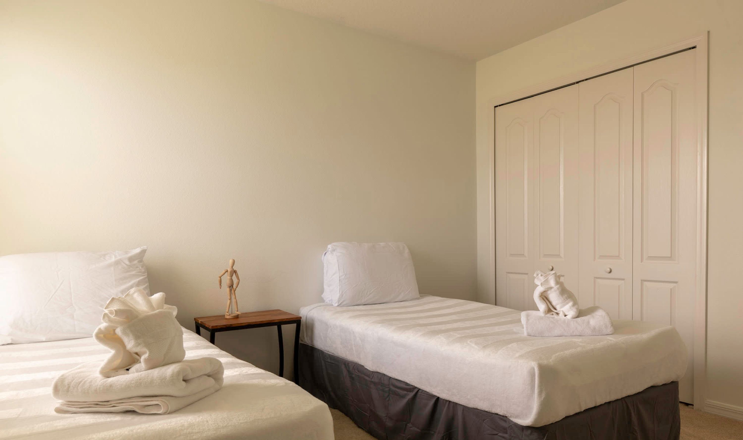 A hotel room with two beds, a wooden nightstand, a small table, and a wardrobe.