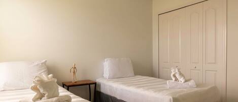 A hotel room with two beds, a wooden nightstand, a small table, and a wardrobe.