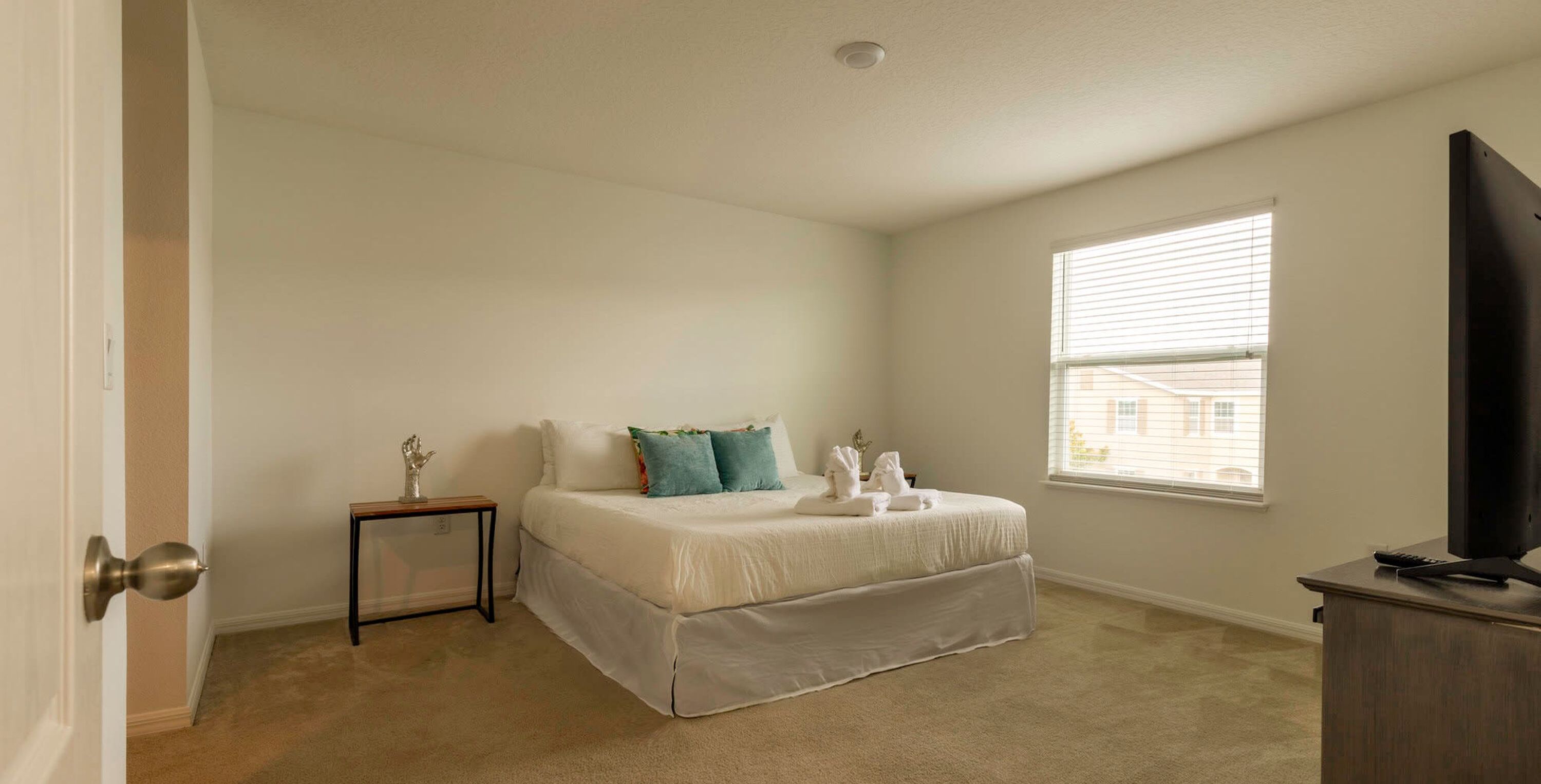 A bedroom with a bed, a small bedside table, a window, and a TV stand.